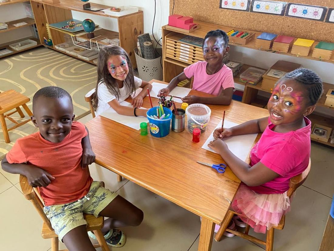 Four smiling children drawing together at a table in the Montessori classroom