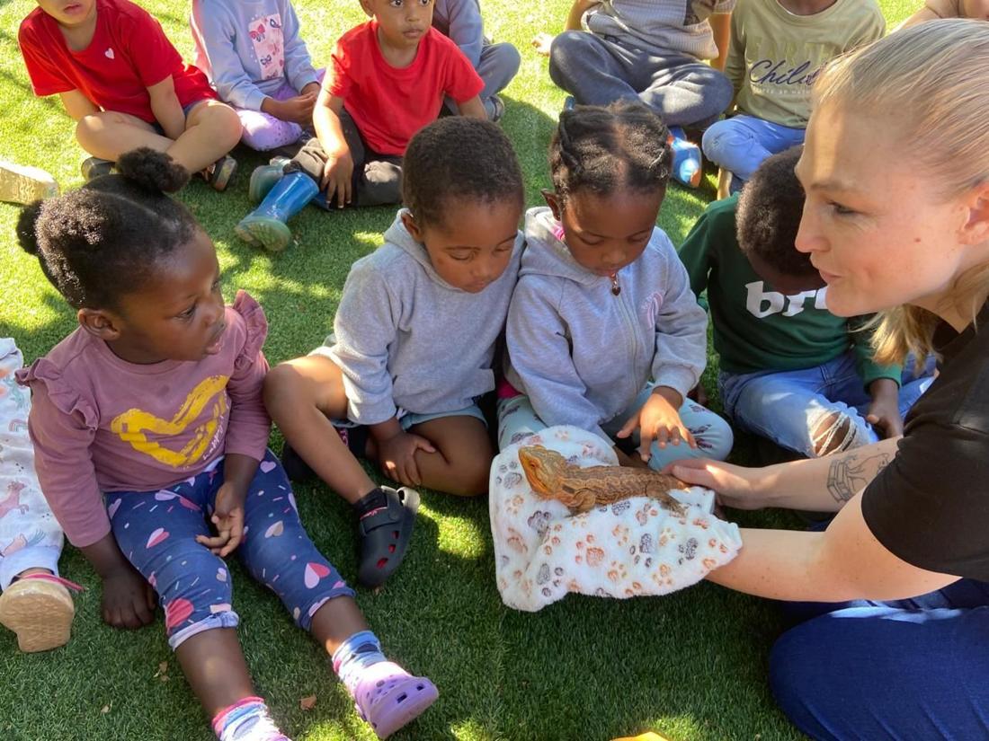 Children sitting on the grass meeting a bearded dragon with a teacher