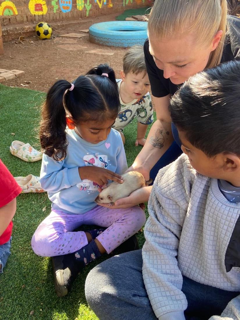 A teacher holds a pet rat while a little girl gently strokes it